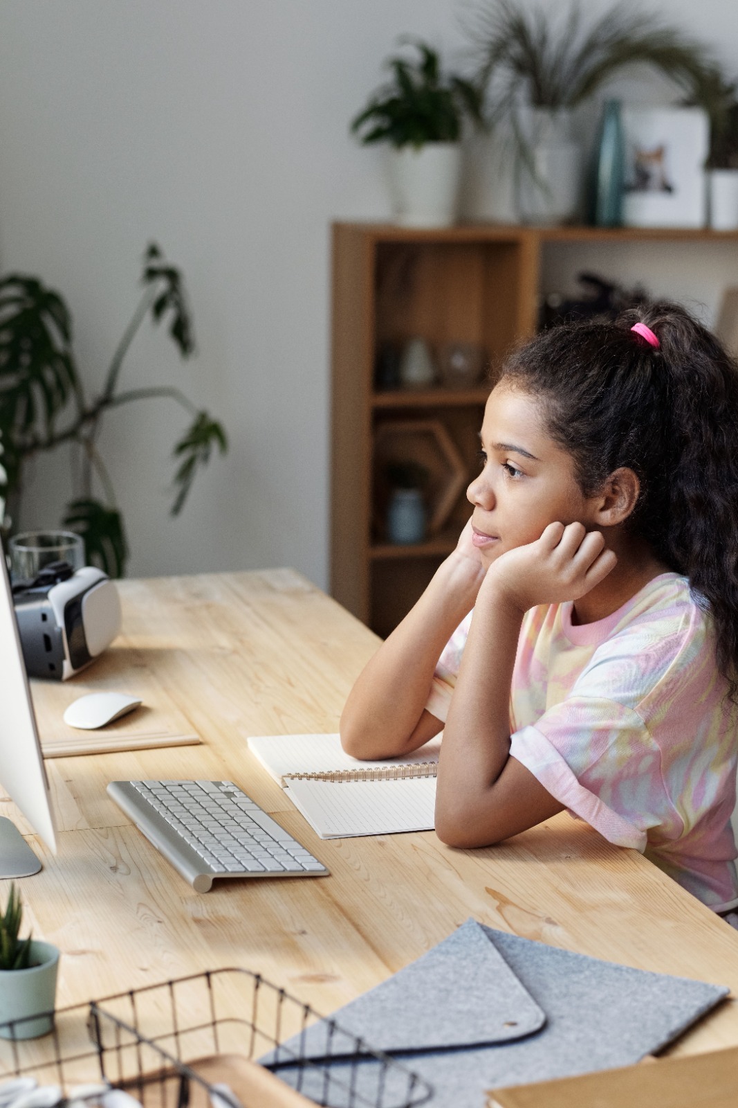 Menina apoiando o rosto nas mãos, olhando para a tela do computador durante uma sessão online